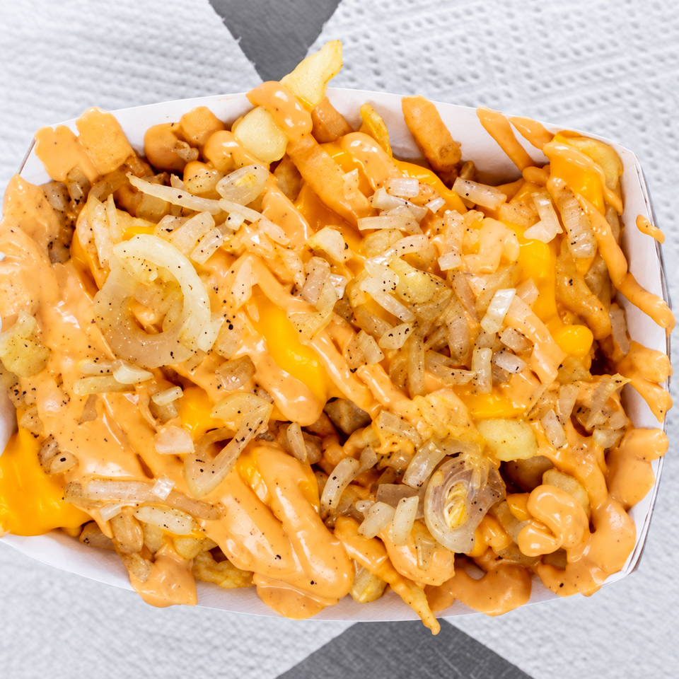 Loaded fries topped with melted cheese, creamy orange sauce, sautéed onions, and pepper in a white serving tray.