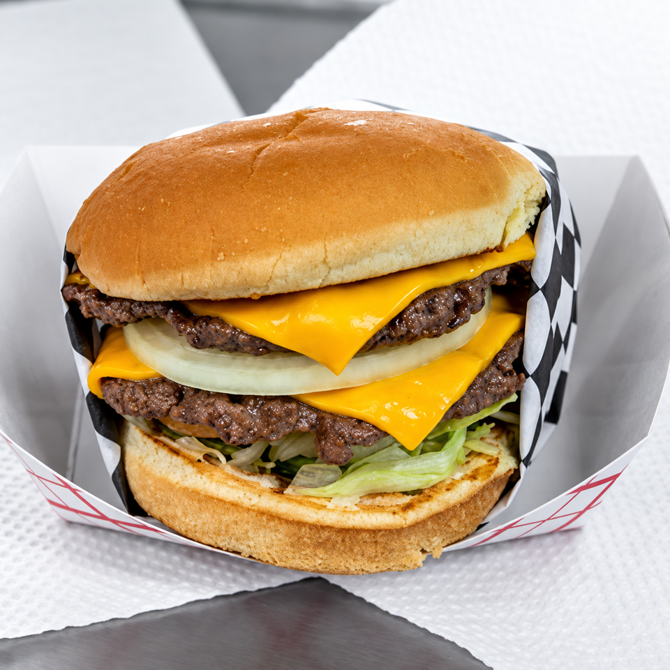 Double cheeseburger with lettuce and onions, served in checkered paper on a white table.